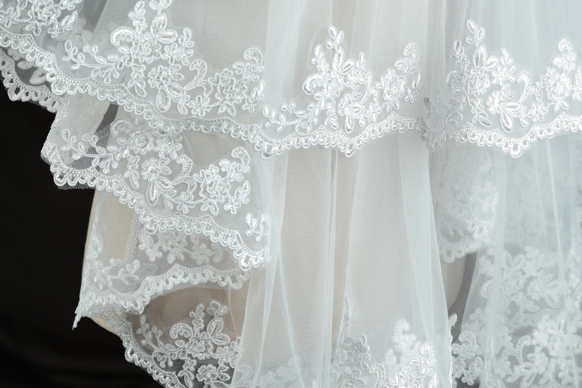 A close-up view of a delicate, white lace wedding dress with intricate floral embroidery.