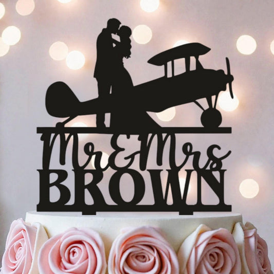 A silhouette of a couple embracing an airplane on a cake topper, with the text "Mr & Mrs Brown" below it.