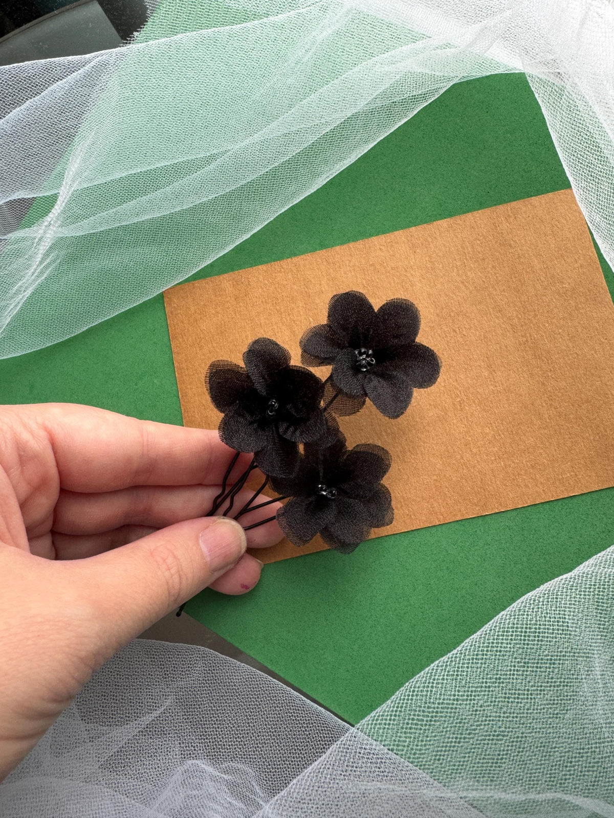 A hand is holding a small bouquet of black flowers against a green background.