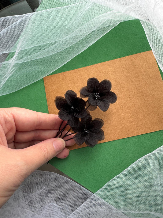 A hand is holding a small bouquet of black flowers against a green background.
