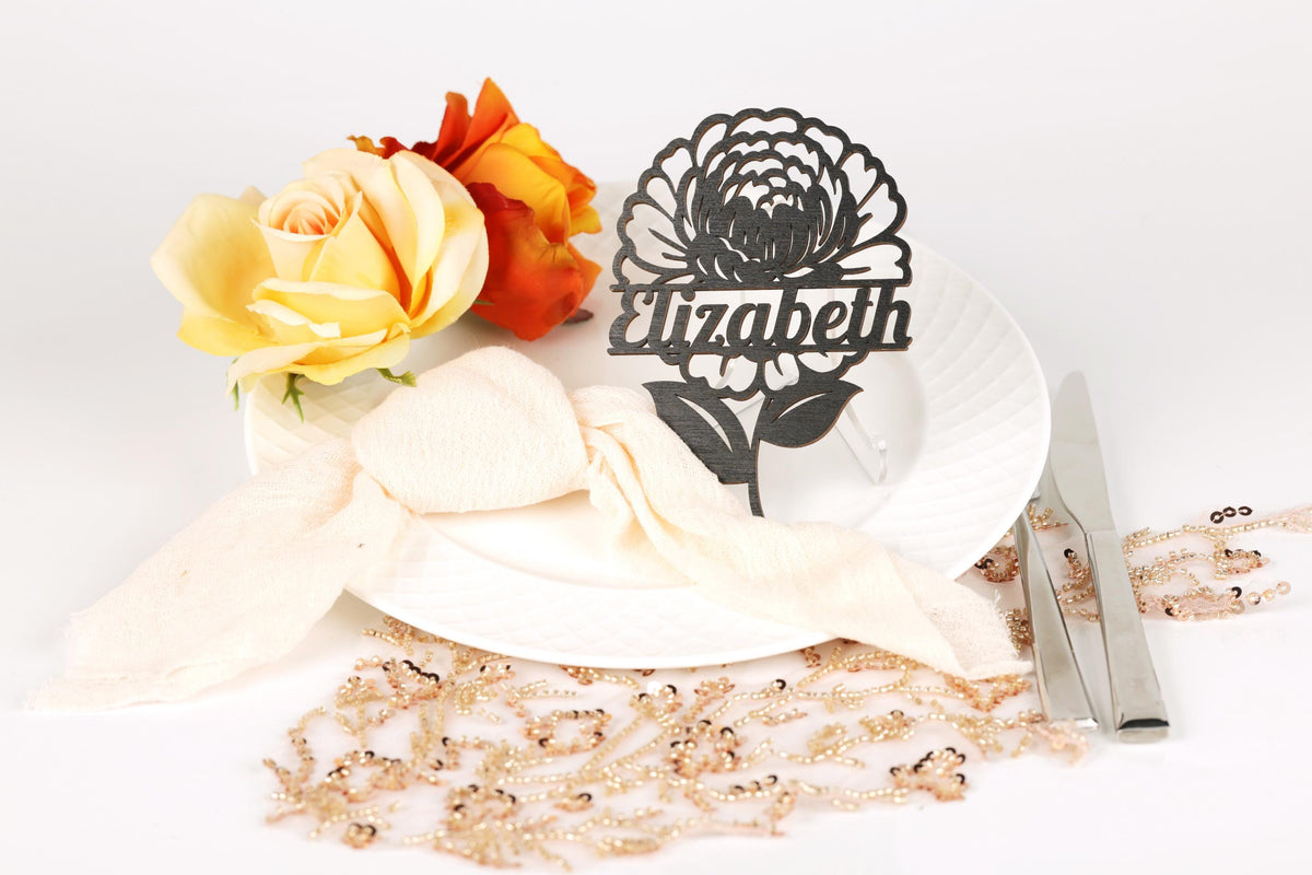 a white plate with a floral design, a bouquet of yellow and orange roses, and a nameplate with a black floral design.