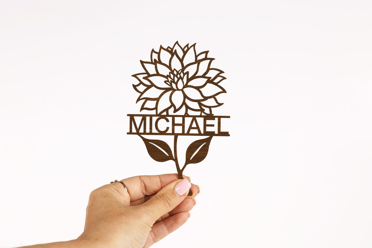 A hand holding a cutout of a flower with the name "MICHAEL" written on it.