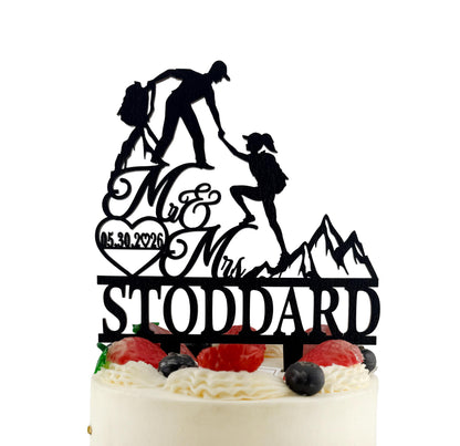 A silhouette of a man and a woman climbing a mountain, with the text "Mr & Mrs STODDARD" on a cake topper.