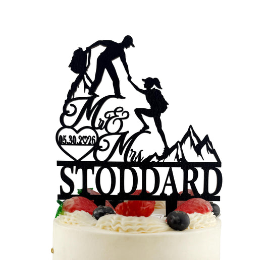 A silhouette of a man and a woman climbing a mountain, with the text "Mr & Mrs STODDARD" on a cake topper.
