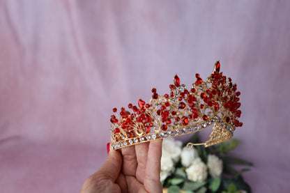 a hand holding a red and gold tiara