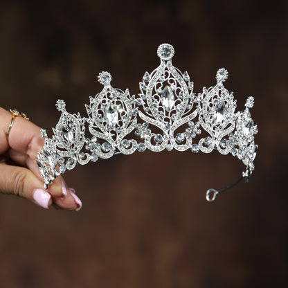 A hand holding a silver tiara adorned with numerous sparkling diamonds.