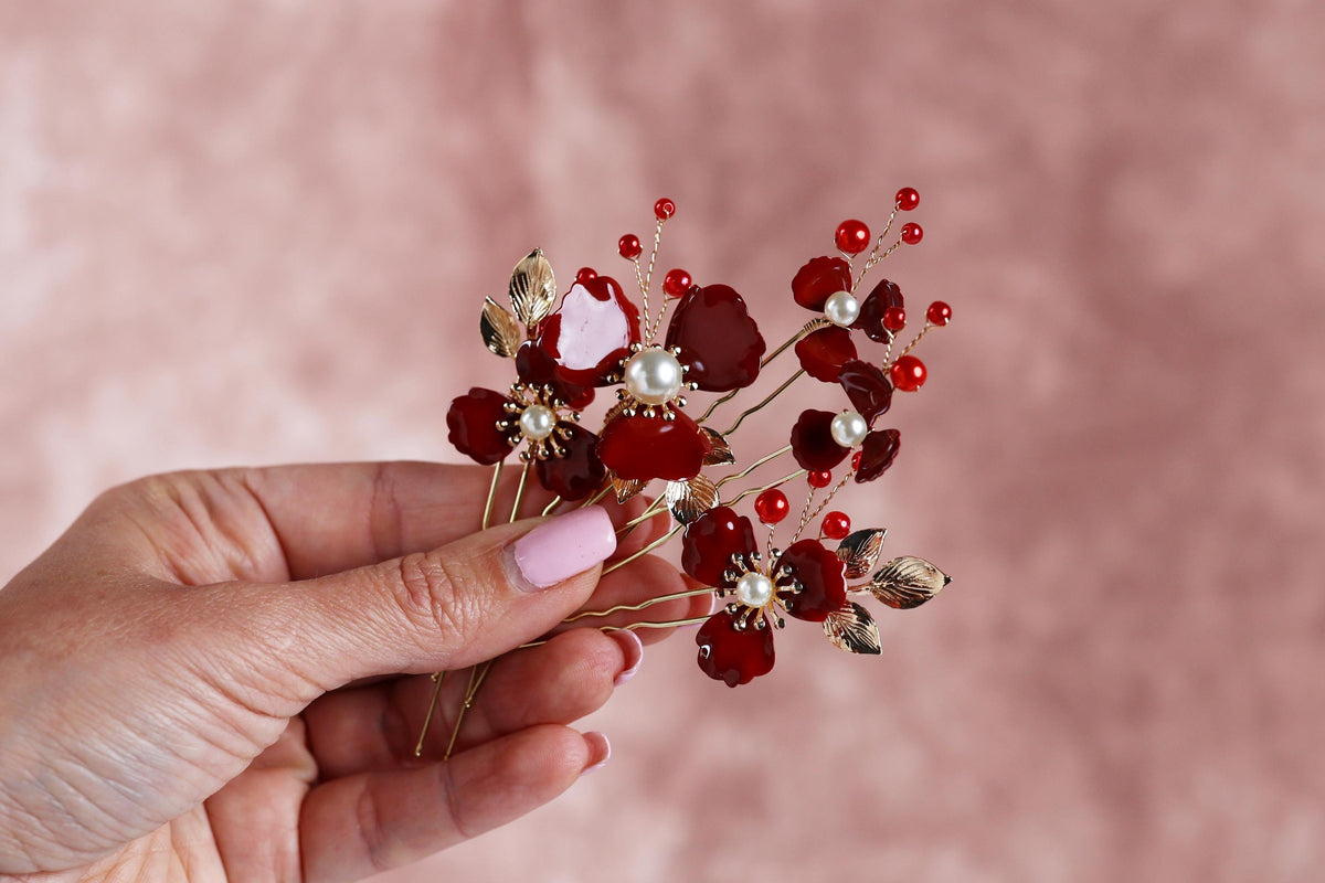A hand holding a decorative hair clip with red and white flowers and gold accents.