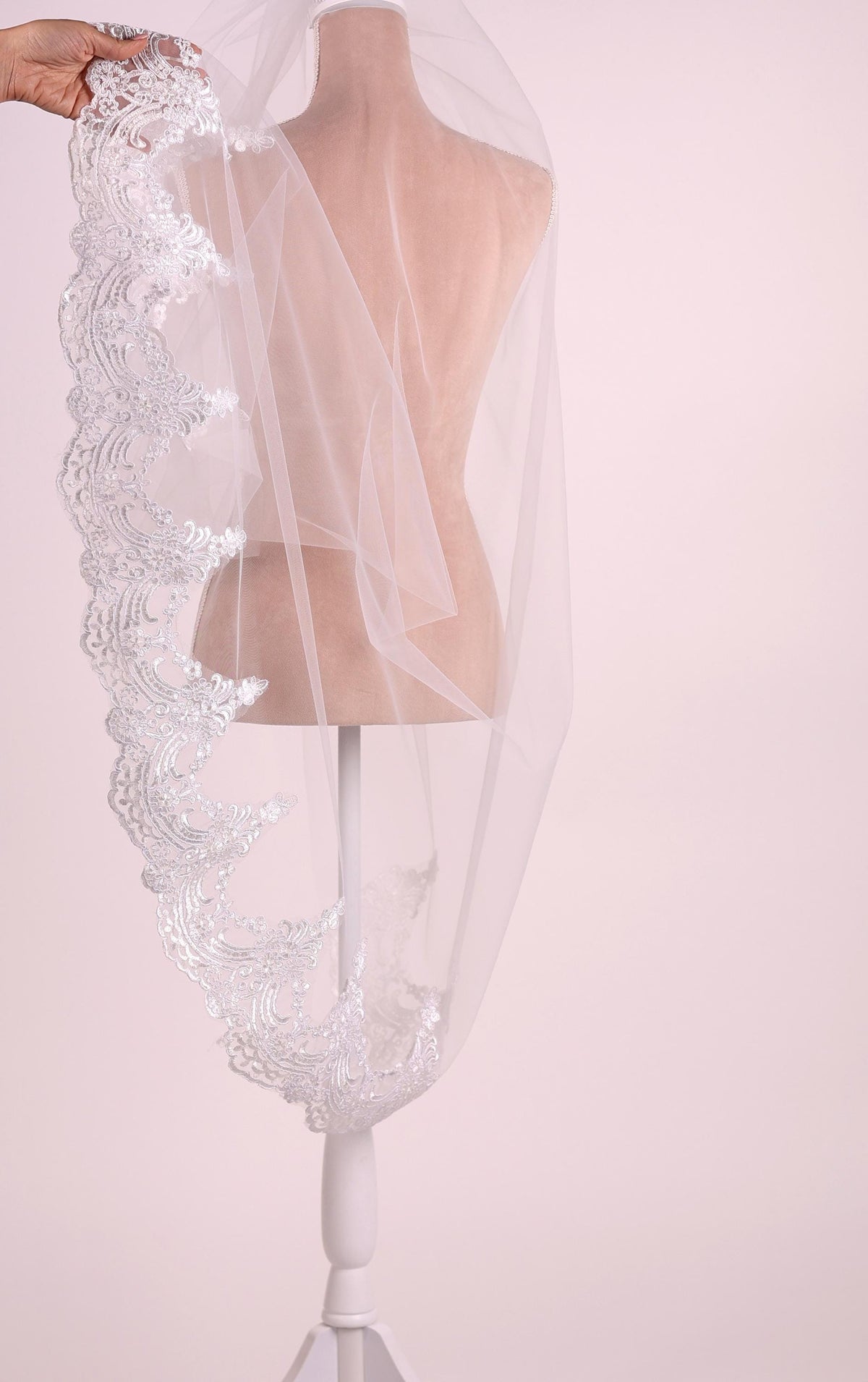 A white mannequin wearing a white veil with intricate lace detailing.