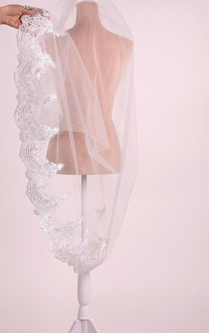 A white mannequin wearing a white veil with intricate lace detailing.