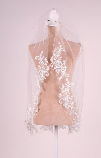 A mannequin wearing a white veil with intricate floral embroidery.