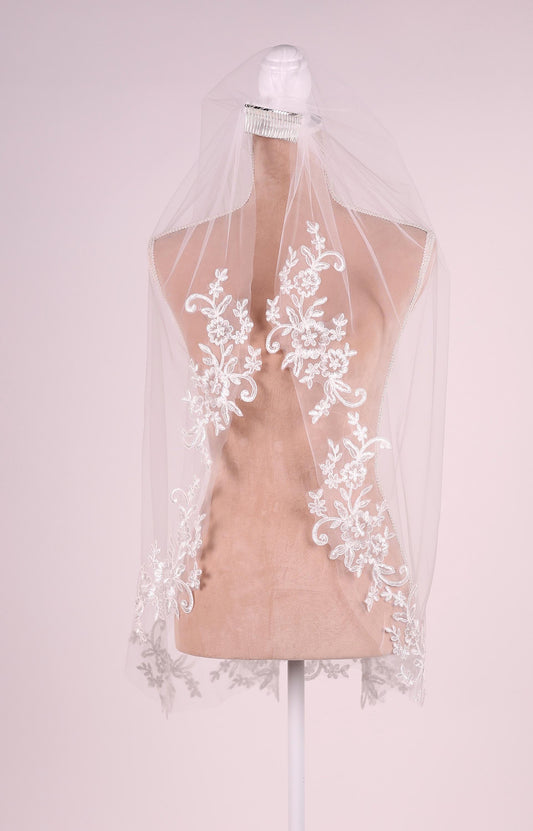 A mannequin wearing a white veil with intricate floral embroidery.