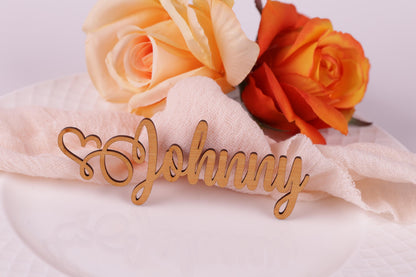 a wooden nameplate with the name "Johny" written on it, placed on a white plate. There are two roses, one orange and one peach, positioned behind the nameplate.