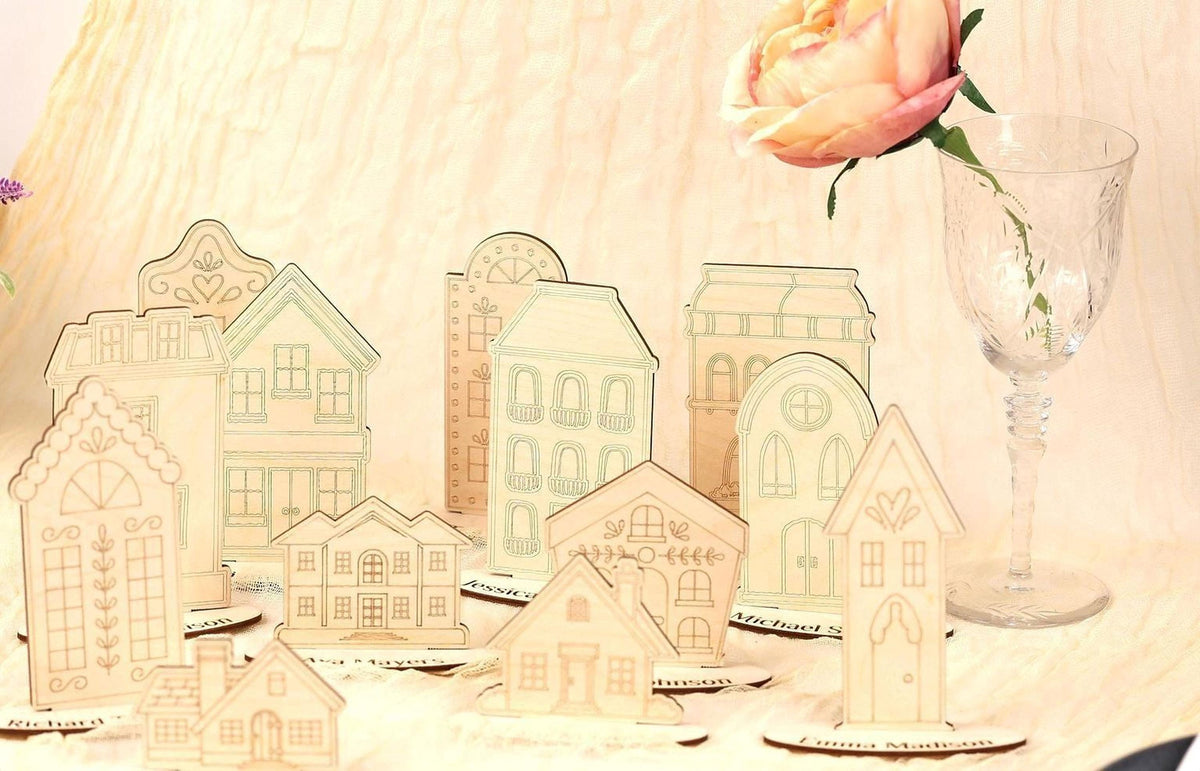 a collection of wooden cutouts of houses, each with unique architectural details, arranged on a table alongside a glass vase with a single pink rose.