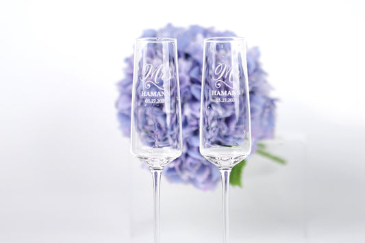 two champagne flutes with personalized messages, placed in front of a bouquet of purple flowers.