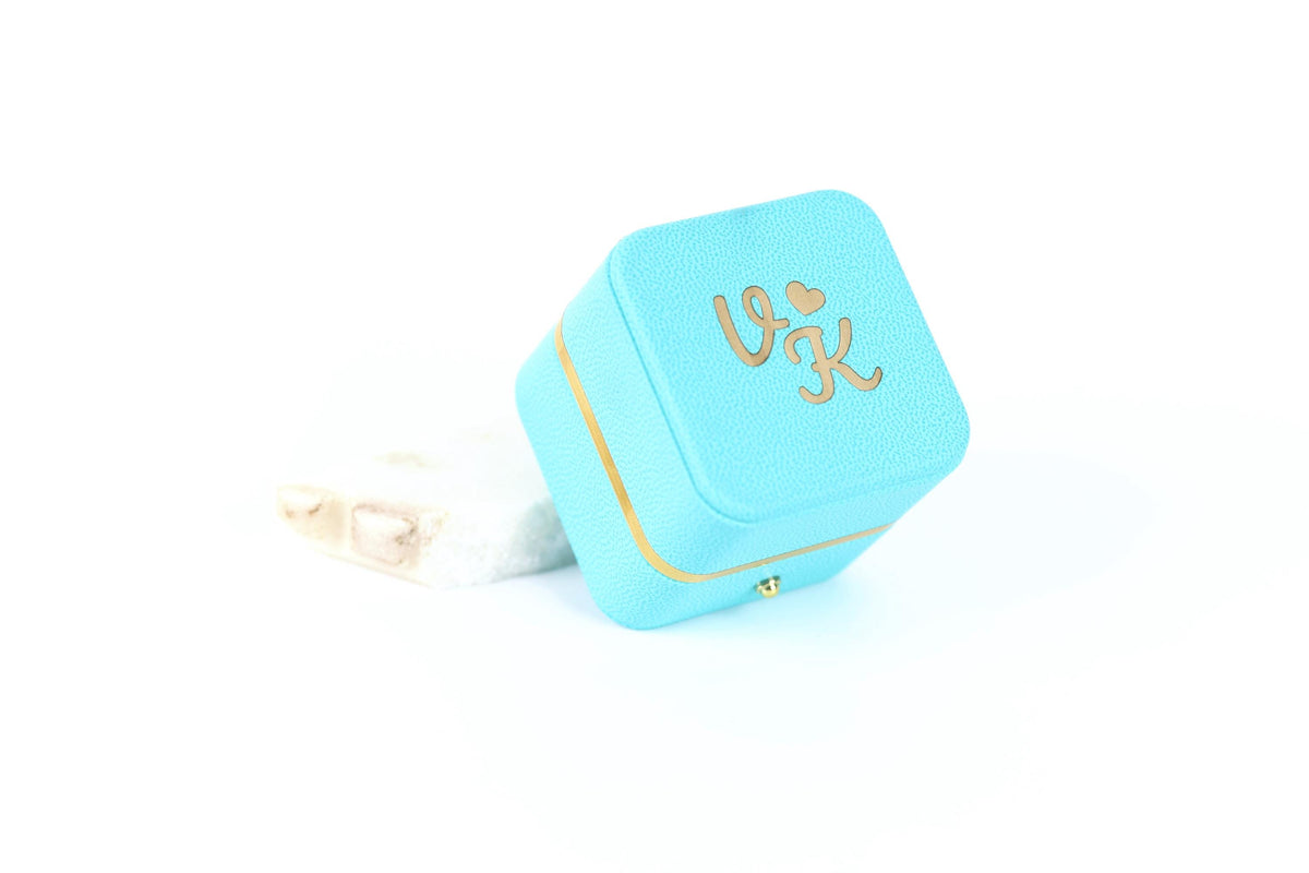 A turquoise jewelry box with the letters 'VK' printed on it, placed on a white surface.