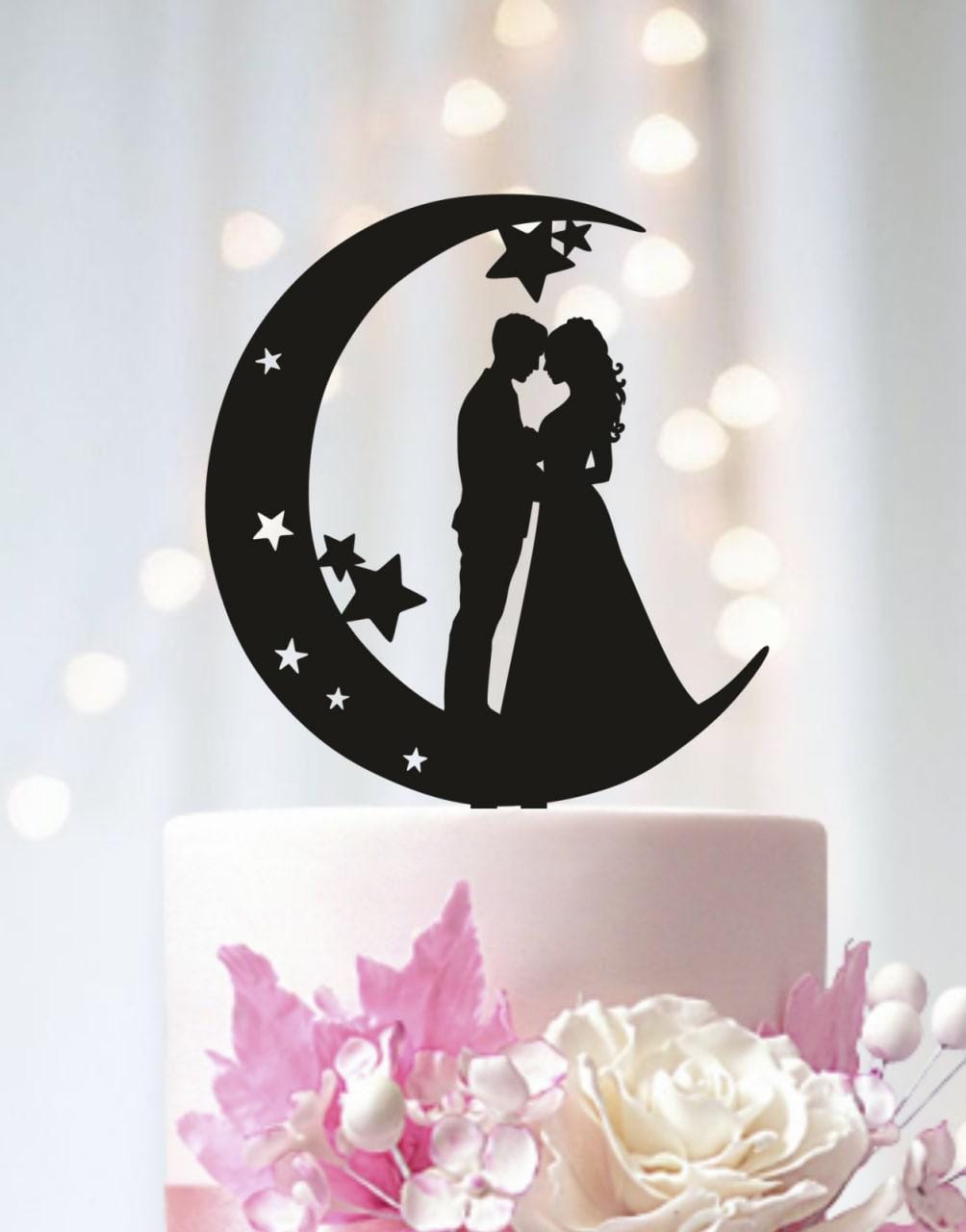 A silhouette of a couple embracing under a crescent moon with stars, serving as a wedding cake topper.