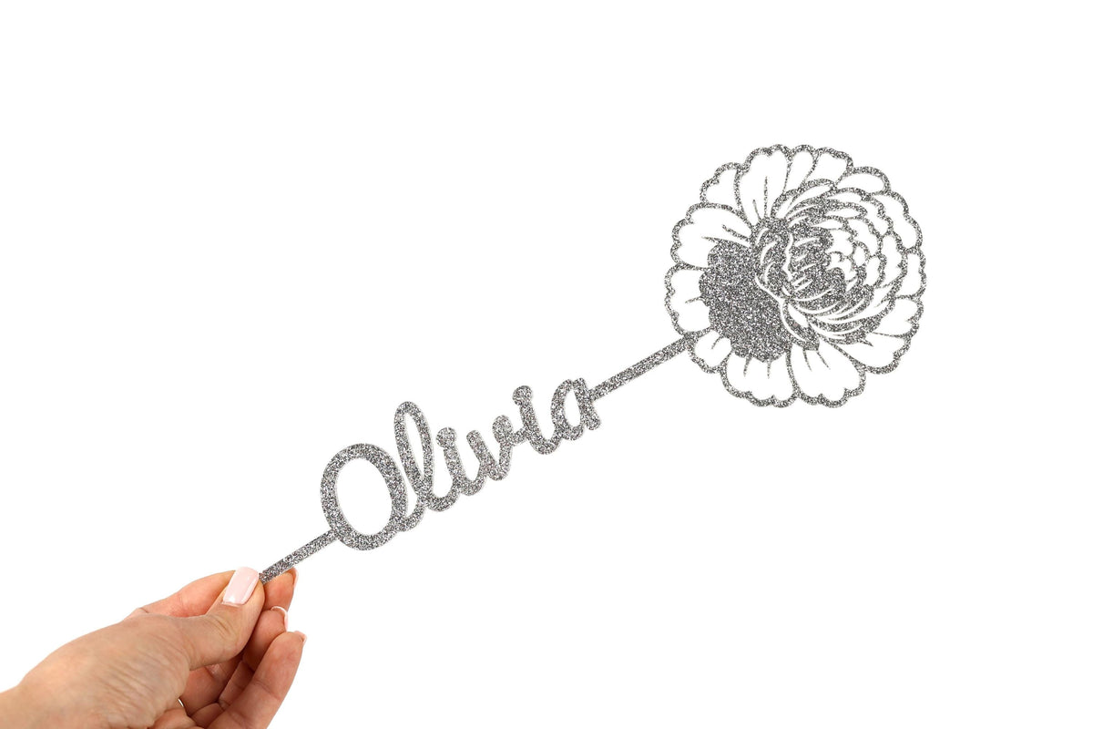 A hand holding a decorative item with the name "Olivia" written on it.