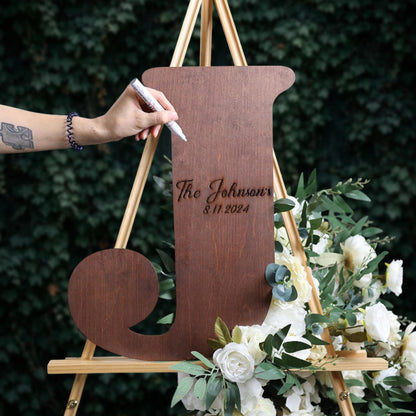 A person is writing on a wooden sign that says "The Johnsons" and "11/11/2024" using a marker.