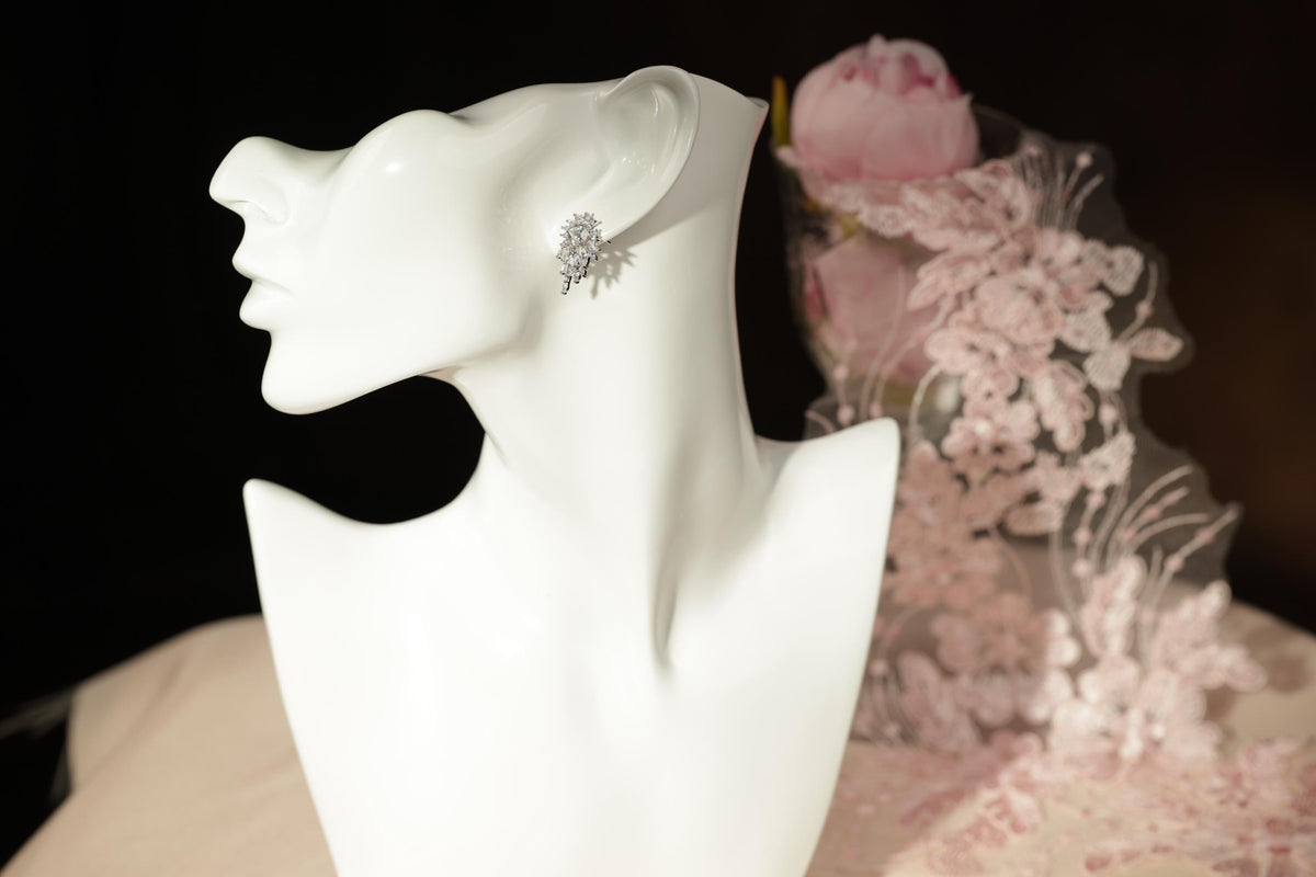 A white bust form with a pair of earrings on it, placed on a table with a pink floral background.