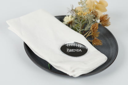 A white napkin with a name tag on it, placed on a black plate with some flowers and dried flowers.