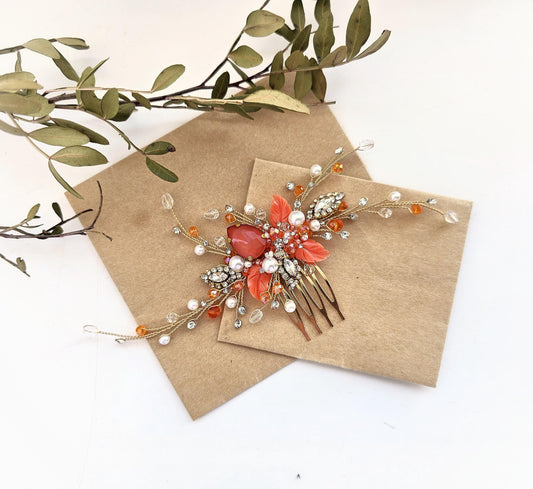 a decorative hair accessory with a floral design, including a red flower and various gemstones, placed on a brown envelope or card.