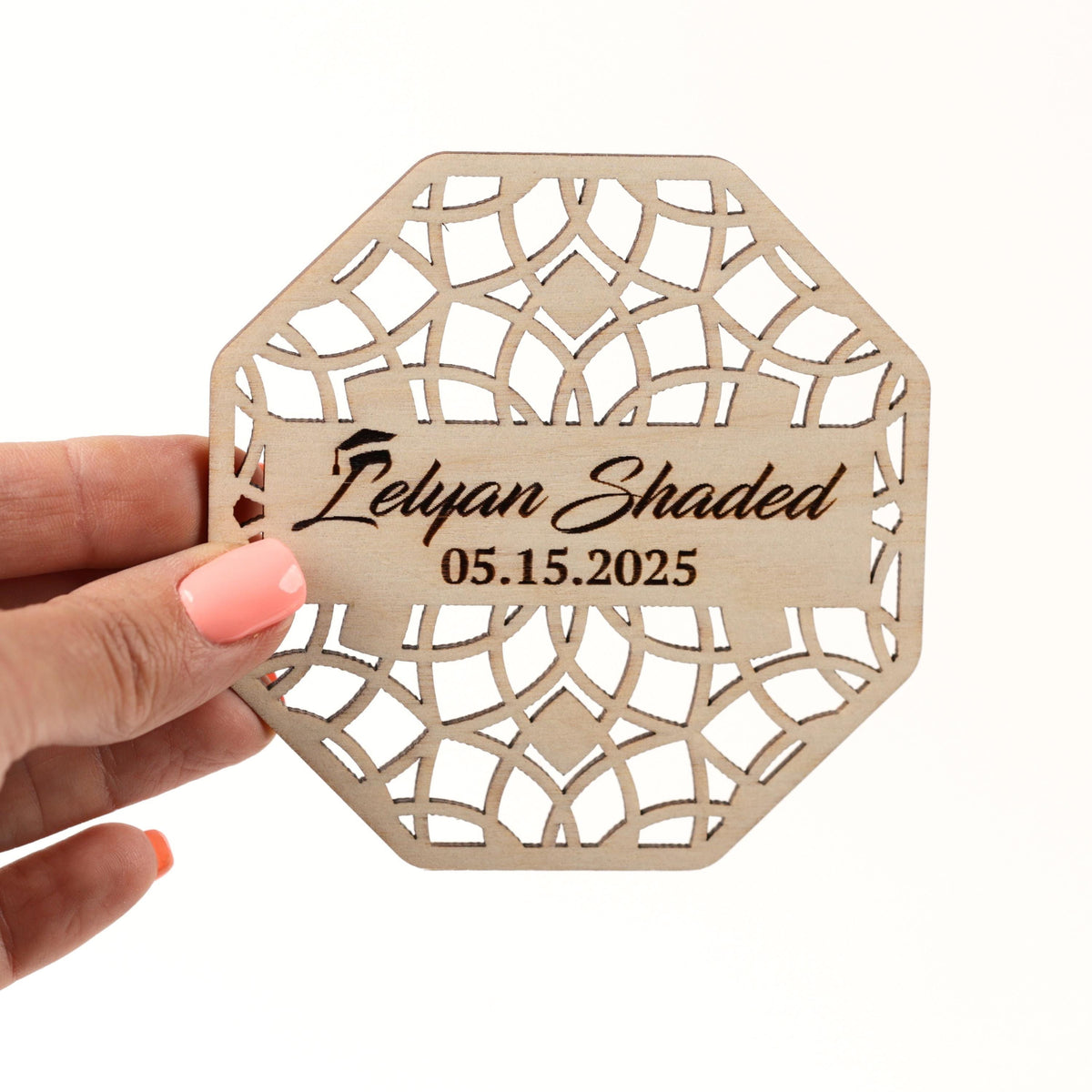 A hand holding a wooden coaster with a laser cut design and text on it.