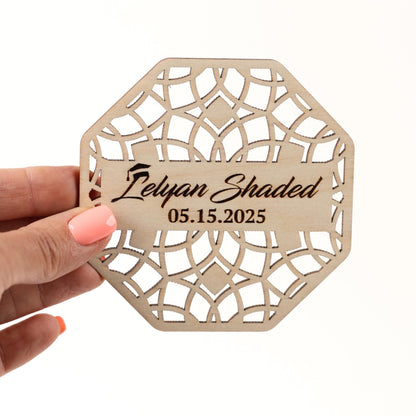 A hand holding a wooden coaster with a laser cut design and text on it.