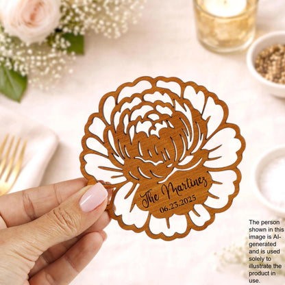 A hand holding a wooden card with a floral design and text on it, with a table setting and other decorative items in the background.
