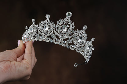 A hand holding a silver tiara adorned with numerous sparkling diamonds.