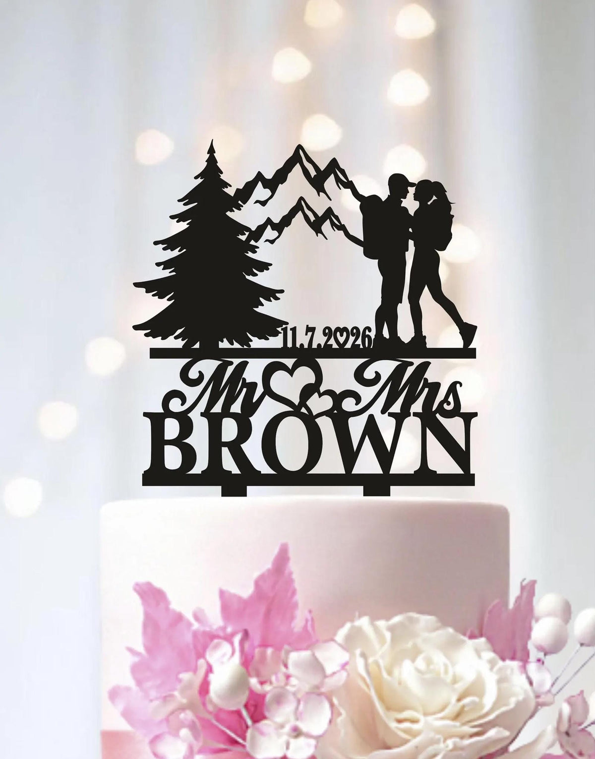 A black silhouette of a couple embracing, with mountains in the background, is displayed on a wedding cake topper.