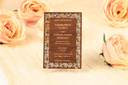 A wooden wedding invitation card with a floral design, placed on a white surface with peach-colored roses in the background.