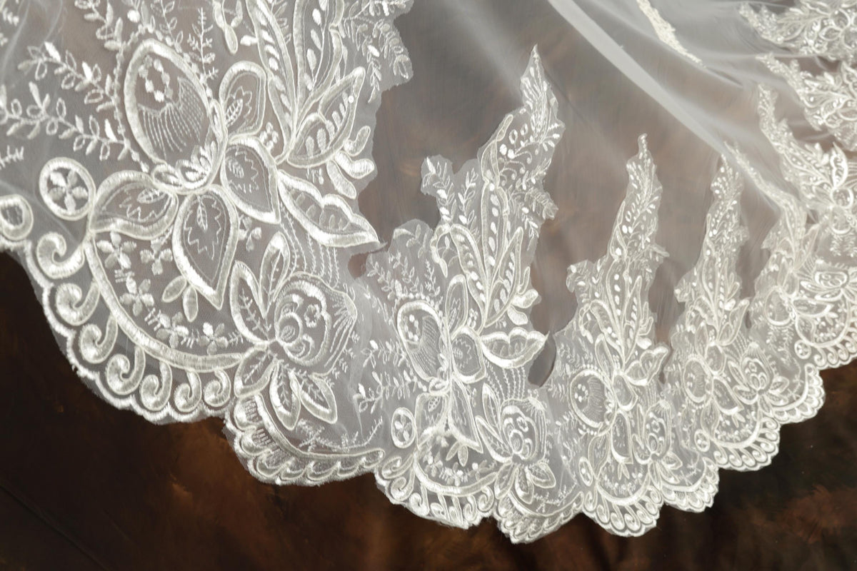 A close-up view of an intricate white lace veil with delicate floral patterns.