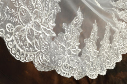 A close-up view of an intricate white lace veil with delicate floral patterns.