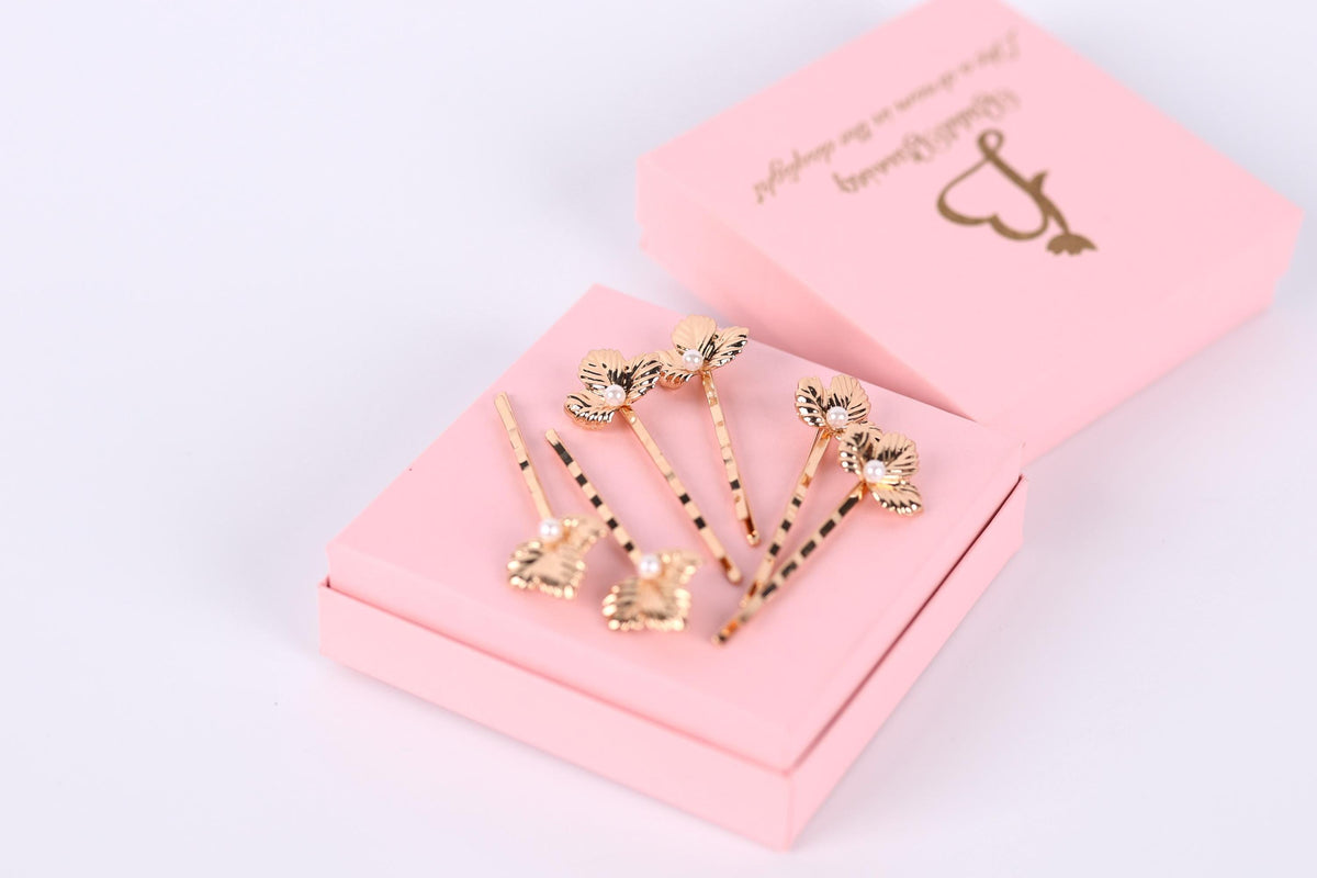 A pink jewelry box containing several gold-colored earrings with floral designs.