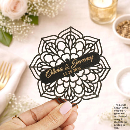 A hand holding a decorative paper with the names 'Olivia & Jeremy' and the date '12.25.25' on it, surrounded by floral decorations and other wedding-related items.