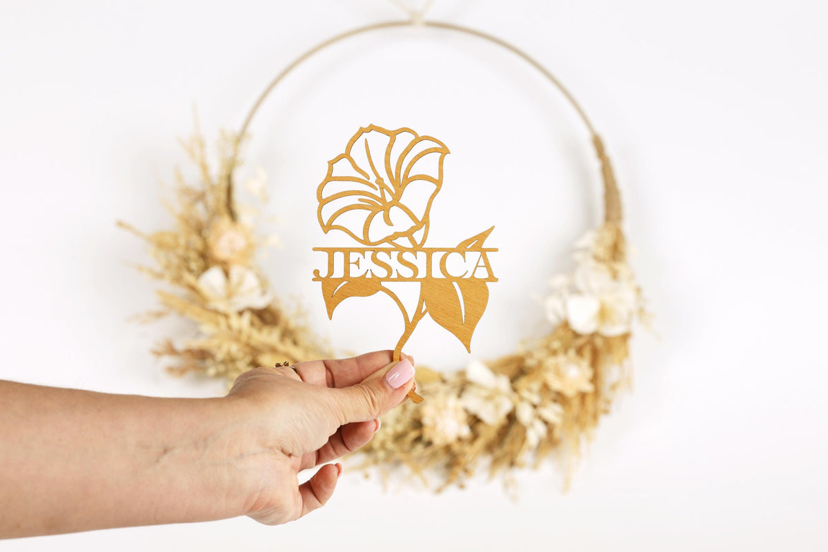A hand holding a piece of paper with a gold flower design and the name "JESSICA" written on it.