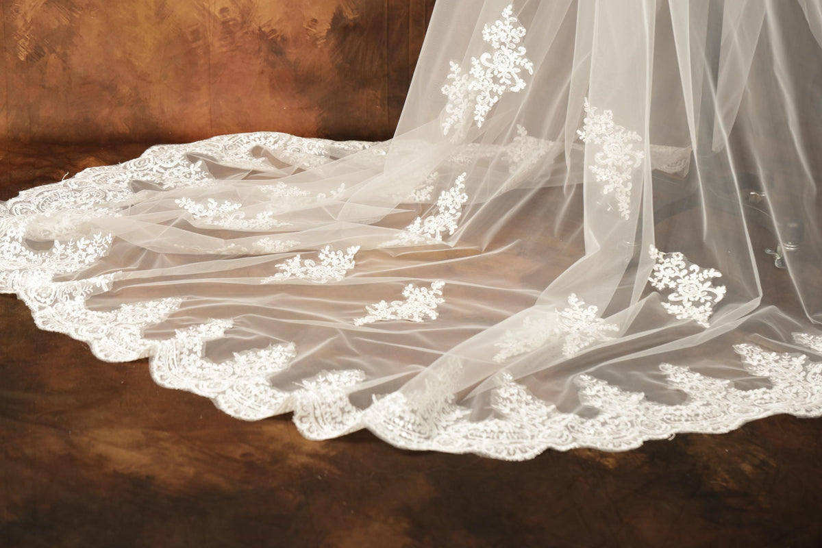 A close-up view of a delicate white lace veil with intricate floral embroidery, partially draped over a wooden surface.