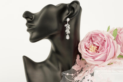 A black mannequin head wearing a pair of dangling earrings with a floral design, accompanied by a bouquet of pink roses.