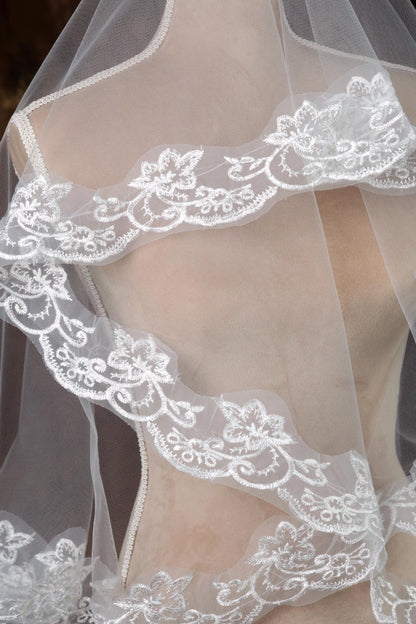 A close-up view of a delicate white lace veil with intricate floral embroidery.