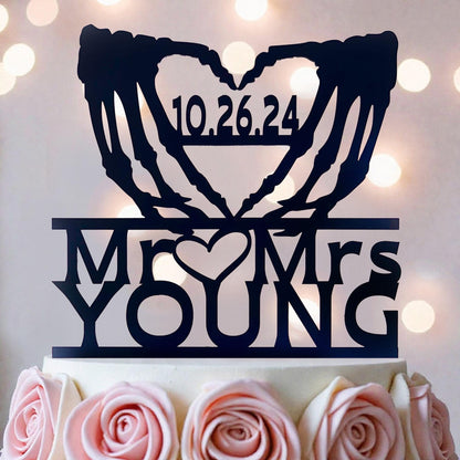 A black silhouette of a heart with the text "10.26.24" and "Mr. YOUNG" written on it, placed on top of a white cake decorated with pink roses.