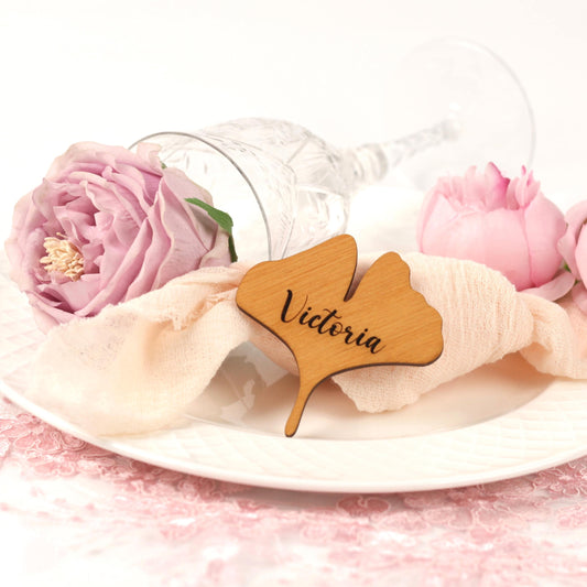 a table setting with a glass, a pink rose, a wooden name tag, and a lace tablecloth.
