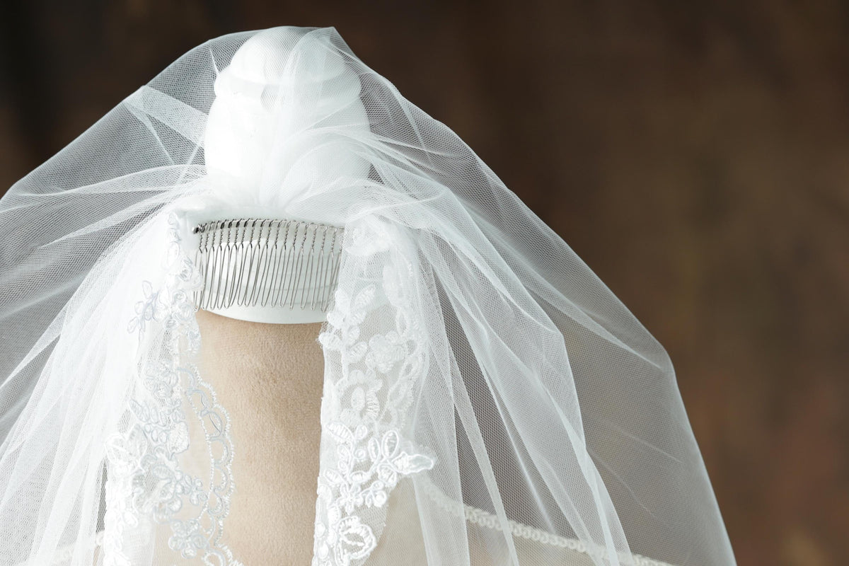 A white veil with intricate lace details is draped over a mannequin head, creating a delicate and elegant appearance.