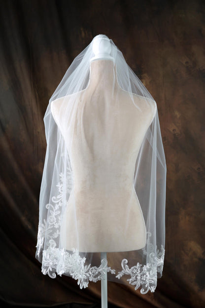 A white mannequin wearing a white veil with intricate lace detailing.