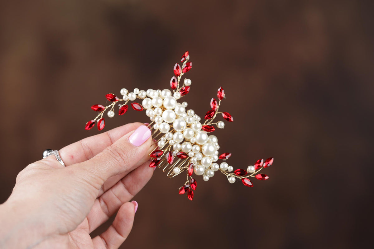a hand holding a red and white flower brooch