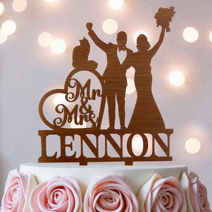 A wooden wedding cake topper featuring silhouettes of a bride and groom, with the name "Lennon" written on it.