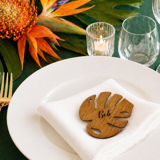 a white plate with a wooden leaf-shaped name tag on it, placed on a table with a green tablecloth.