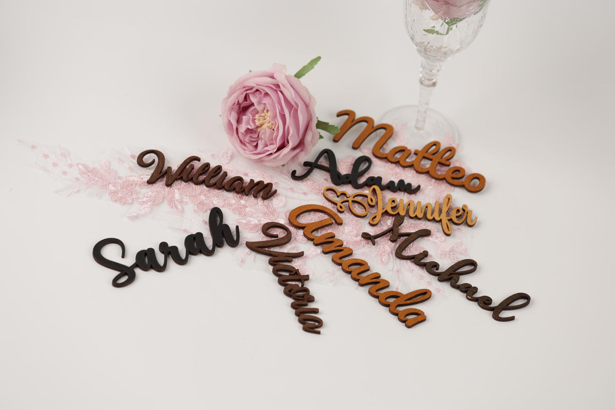 a collection of wooden name cards with names written on them, along with a pink rose and a wine glass.