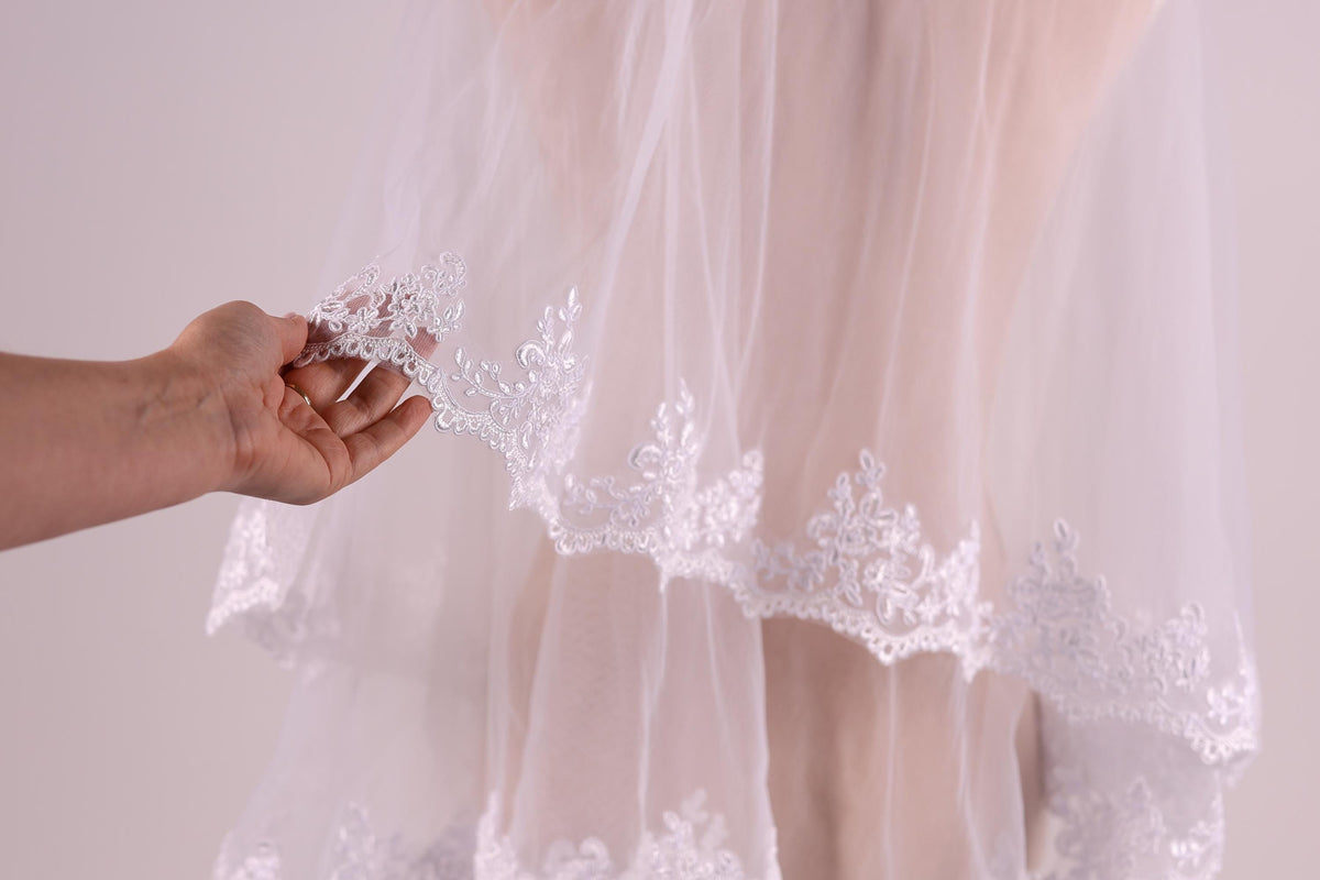 A hand holding a piece of white lace on a veil.