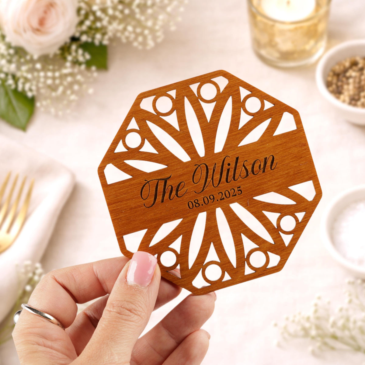 A hand holding a wooden coaster with the name 'The Wilson' and the date '08.09.2025' printed on it.