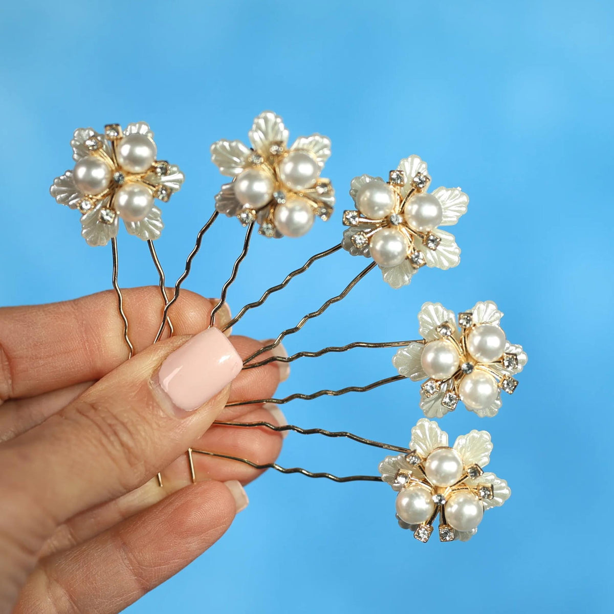 A hand holding a group of six white pearl-like hair clips against a blue background.